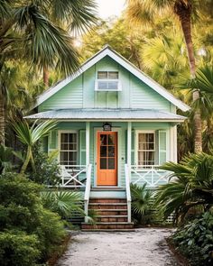 a blue house surrounded by palm trees and greenery with a bright orange front door