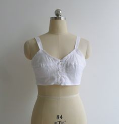 "Brand new vintage deadstock from the 1970's. Soviet era white longline bra top in 100% cotton. Features darted bra cups with circle stitching to the bottom half, slim shoulder straps & a sweet picot trim to the bustline. Closes with a column of buttons to the center front. Could be worn as an undergarment, or even as a cropped camisole top. 100% cotton takes dye well & could be a fun project too! Check out other brassieres in the shop - www.etsy.com/shop/fivestonesvintage?section_id=100