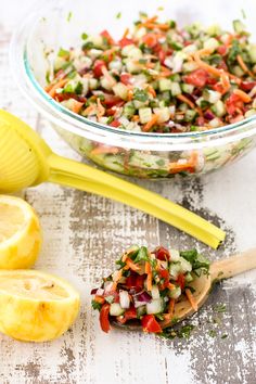 a salad in a glass bowl with a wooden spoon next to it and sliced lemons