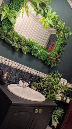 a bathroom with green plants on the wall and a mirror over the sink that has it's reflection