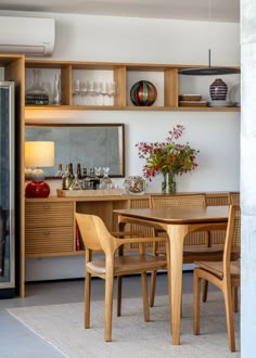 a dining room table and chairs in front of a shelf with wine glasses on it