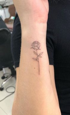 a woman's wrist with a single rose tattoo on it, in the middle of her left arm