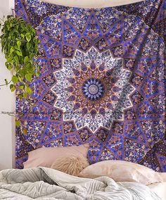 a bed with a purple and pink tapestry hanging on it's wall next to a potted plant