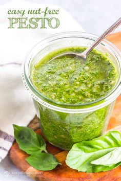 a glass jar filled with pesto sitting on top of a cutting board next to basil leaves