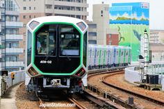 a green and white train traveling down tracks next to tall buildings in the city with lots of windows