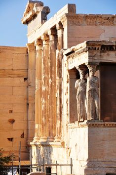 two statues on the side of a building in front of a wall with columns and pillars