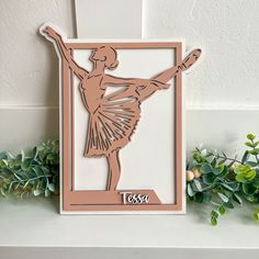 a paper cut out of a ballerina on a shelf next to some green plants