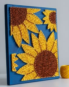 a string art sunflower on a blue board next to a yellow spool of yarn