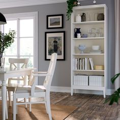 a white dining room table and chairs in front of a bookshelf with pictures on the wall