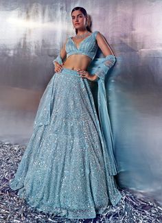 Embrace the elegance with the Blue Sequins Embroidered Bridal Lehenga Set, a true masterpiece of craftsmanship and sophistication. Crafted from soft net fabric, the flowing blue lehenga is meticulously adorned with tonal sequins, crystals, and hand-dyed pearls, creating a mesmerizing shimmer that captivates with every step. The intricate embroidery elevates the ensemble’s luxurious appeal, ensuring you make a statement as you grace your special day. Teamed with a matching blouse featuring exquisite embroidery, and completed with a delicate dupatta bordered to perfection, this set exudes timeless grace. Ideal for the bride or bride-to-be, this outfit is designed to make your wedding day unforgettable. Composition : Lehenga, Blouse and Dupatta - Net Care: Dry Clean Only and Vacuum Storage Th Blue Net Lehenga, Color Tiffany, Embroidered Bridal Lehenga, Set Saree, Blue Lehenga, Vacuum Storage, Net Lehenga, Sharara Set