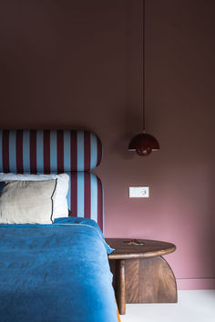 a bed with blue sheets and pillows next to a red lamp hanging from the ceiling