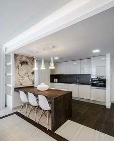 a modern kitchen with white cabinets and wood flooring, along with an art work on the wall