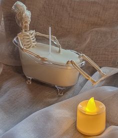 a candle that is sitting next to a fake skeleton in a bathtub on a bed