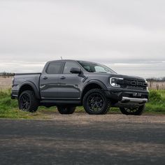 a grey truck parked on the side of a road next to a grass covered field