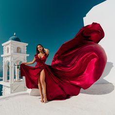 a woman in a red dress standing on the roof of a white building with a bell tower behind her