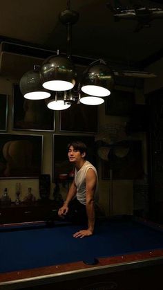 a man standing on top of a pool table in front of two hanging light bulbs