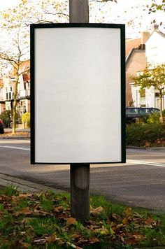 an empty sign on a pole in the grass next to a street with houses and trees