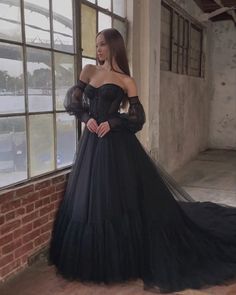 a woman standing in front of a window wearing a black dress with long sleeves and sheer neckline