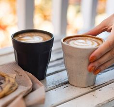 two cups of coffee sitting on top of a wooden table