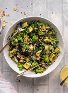 a bowl filled with broccoli, raisins and nuts next to a carton of orange juice