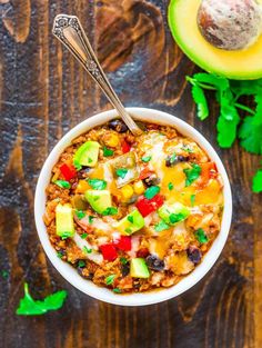 a white bowl filled with chili and avocado on top of a wooden table