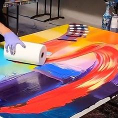 a person in white gloves is painting on a large sheet of paper with colorful colors