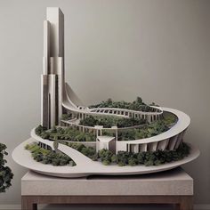 an architectural model of a building surrounded by trees and bushes on a table next to a potted plant