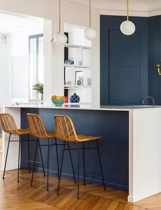 two bar stools sit in front of an island with blue walls and wooden floors