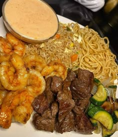 a white plate topped with meat and veggies next to noodles, sauce on top