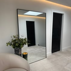 an empty room with a large mirror on the wall next to a white chair and potted plant