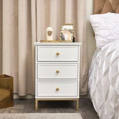 a white dresser sitting next to a bed with a gold frame on top of it