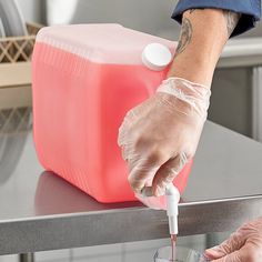 a person in gloves and latex gloves is filling a container with liquid from a jug