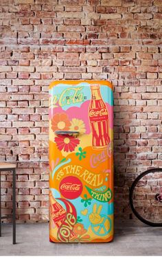 a brightly colored refrigerator next to a brick wall with a bicycle parked in front of it