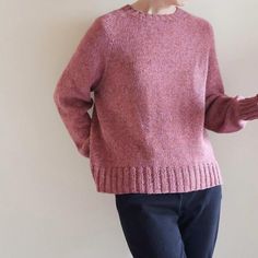 a woman standing in front of a white wall wearing a pink sweater