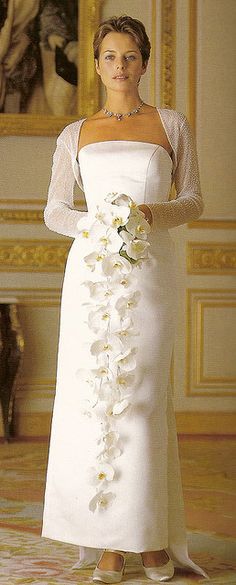 a woman in a white dress with flowers on the side and her hands behind her back