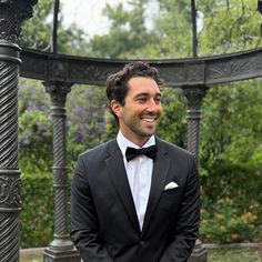 a man in a tuxedo smiles at the camera while standing under a gazebo