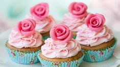 several cupcakes with pink frosting and roses on them sitting on a plate