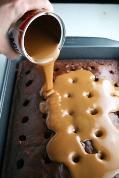 a person pouring caramel sauce on top of a chocolate cake in a baking pan