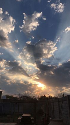 the sun is setting behind some clouds in the sky over a fenced area with benches