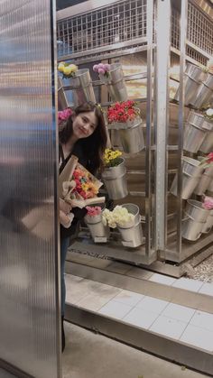 a woman standing in front of a display case filled with lots of potted flowers