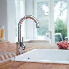 a kitchen sink sitting on top of a wooden counter next to a bowl of fruit