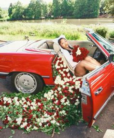 a woman laying in the back of a red car with flowers all over her body