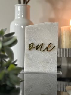 a white card with the word one written in gold on it next to some candles