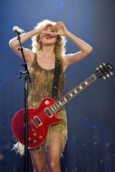 a woman holding a red guitar in front of her face and wearing a gold dress