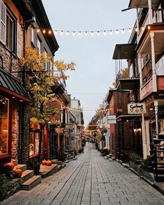 an empty street lined with brick buildings and lights strung from the ceiling above it are pumpkins