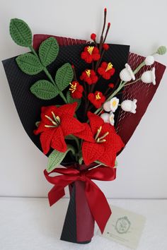 a bouquet of flowers is wrapped in red ribbon and placed on top of a black vase