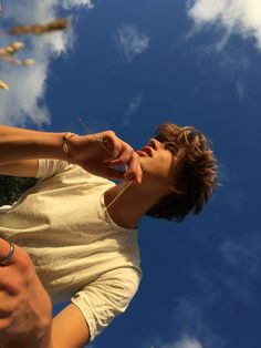 a man holding something in his hand and looking up into the sky with clouds behind him