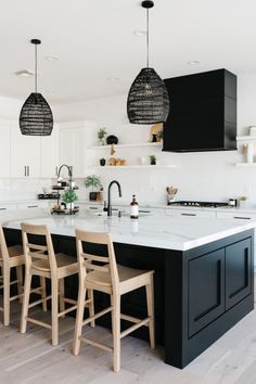 a kitchen with black cabinets and white countertops, two pendant lights above the island