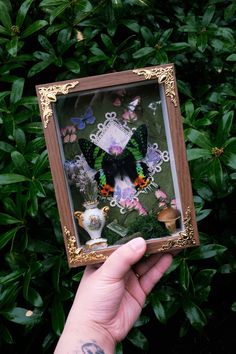 a hand holding up a small frame with a butterfly on it's side and butterflies in the background