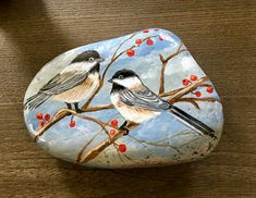 two birds sitting on a branch painted on a rock with red berries and blue sky in the background